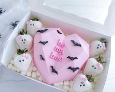 a box filled with lots of white chocolate covered in pink frosting and bats on top