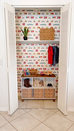 an open closet with clothes and baskets on the shelves, next to a wallpapered wall