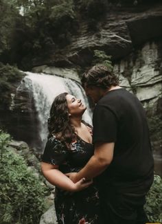 a man and woman standing in front of a waterfall looking at each other with their eyes closed