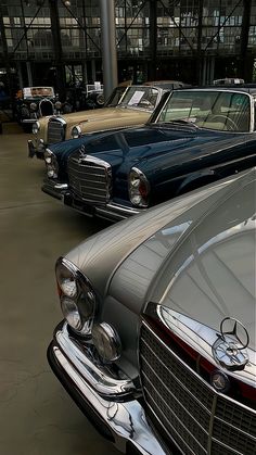 several old mercedess are parked in a garage with glass walls and windows behind them