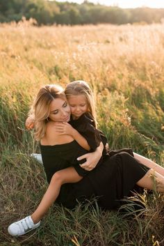 a mother and her daughter are sitting in the tall grass with their arms around each other