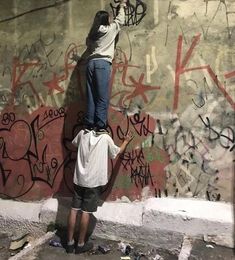 two people painting graffiti on the side of a wall