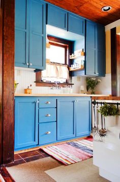 a kitchen with blue cabinets and white counter tops, along with a rug on the floor