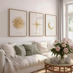 a living room filled with white furniture and paintings on the wall above a coffee table