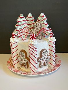 a decorated christmas cake on a plate with candy canes and gingerbread cookies in the shape of houses