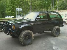 a large black truck parked on top of a parking lot next to a wooded area