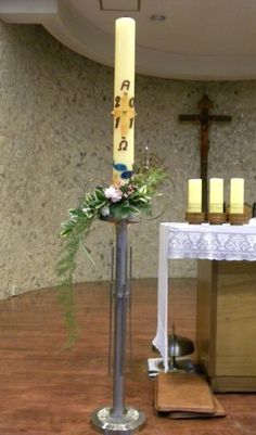 a tall metal candle with flowers on it in front of a cross and other altar decorations