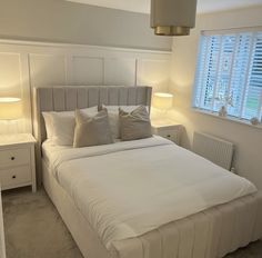 a bed with white sheets and pillows in a bedroom next to two lamps on either side of the bed