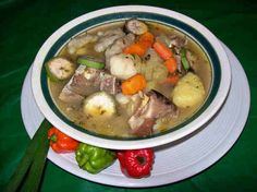 a white bowl filled with meat and vegetables on top of a green tablecloth covered table