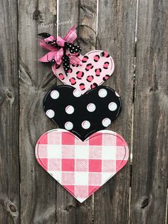 three heart shaped magnets are hanging on a wooden fence with pink and black checkered fabric