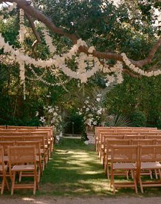 rows of wooden chairs set up for an outdoor wedding ceremony with white flowers and greenery