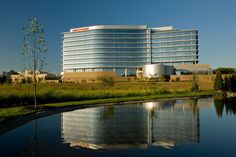 a large building sitting next to a body of water in front of a lush green field