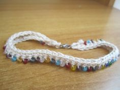 a white crocheted necklace with multicolored beads on a wooden table top