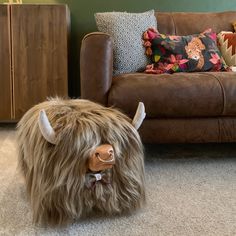 a stuffed yak is sitting on the floor in front of a couch and pillows