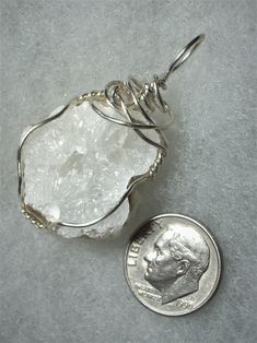 a coin is sitting next to a wire wrapped pendant on a piece of silver foil