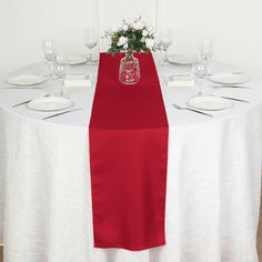 the table is set with white plates and wine glasses, red runner, and a vase filled with flowers