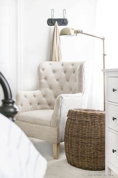 a white chair sitting next to a bed in a bedroom under a light on a wall