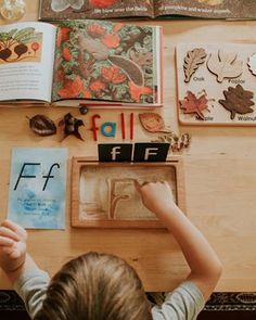 a young boy is playing with some paper and magnets on a wooden table in front of an open book