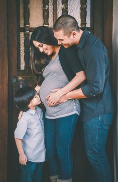 a pregnant woman and two young boys standing in front of a door with their arms around each other