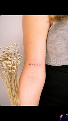 a woman's arm with the word grateful written on it and flowers in front of her