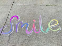 the word smile written in colored chalk on concrete with sidewalk marking it's name