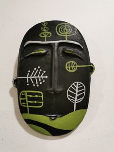 a black mask with green and white designs on it's face hanging from a wall