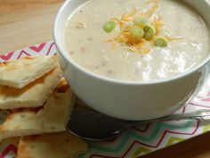 a bowl of soup with crackers and cheese on the side sitting on a plate