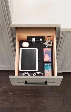 an open drawer with various electronics and cords in it on top of a wooden floor