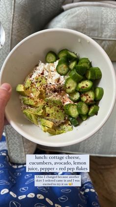 a person holding a white bowl filled with cucumber and other food on top of it