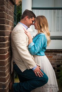 a man and woman standing next to each other in front of a brick wall with their arms around each other