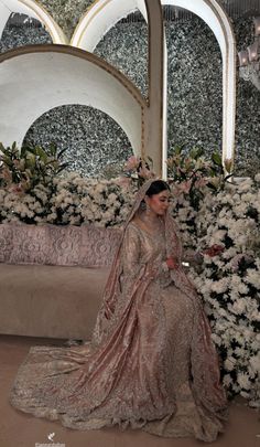 a woman in a wedding dress sitting on a couch with flowers behind her and an ornate mirror