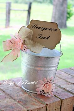 a metal pail filled with pink flowers on top of a wooden table next to a sign