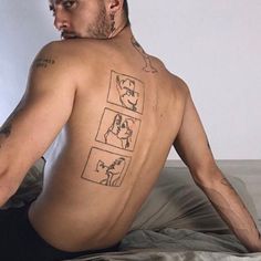 a man with tattoos on his back sitting on a bed and looking at the camera