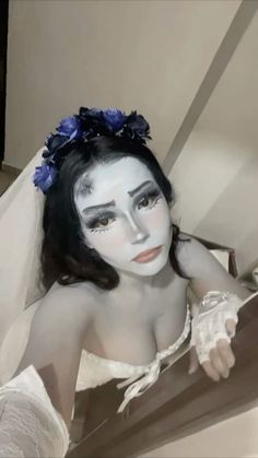 a woman with white makeup and blue flowers on her head is sitting in a chair