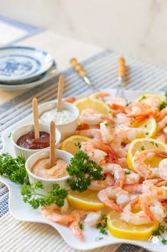 a platter with shrimp, lemon wedges and dipping sauce