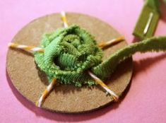 a green flower is sitting on top of a round piece of paper with pins sticking out of it