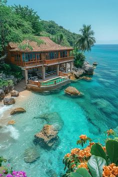 a house sitting on top of a lush green hillside next to the ocean with blue water