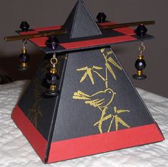 a black and red triangle shaped object with gold designs on it's sides sitting on a bed