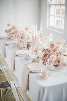 a long table is set with white and pink flowers, silverware and candlesticks