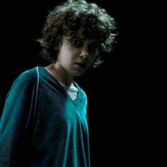 a young boy with curly hair standing in the dark