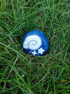 a painted rock sitting in the grass on top of some green grass with white stars