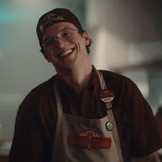 a smiling man wearing an apron and glasses