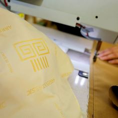 someone is using a sewing machine to sew something on a piece of cloth with yellow lettering