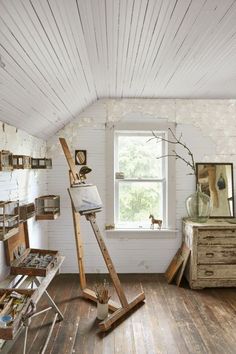 a room with white walls and wooden floors has an easel on the floor in front of a window