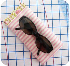 a pair of sunglasses sitting on top of a pink and white striped case next to a ruler