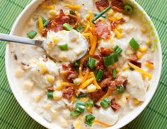 a white bowl filled with potato soup topped with bacon and green onions next to a spoon