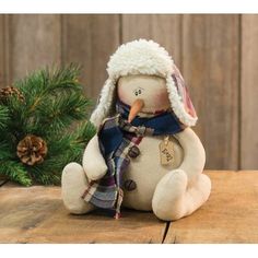 a stuffed snowman sitting on top of a wooden table next to a pine tree