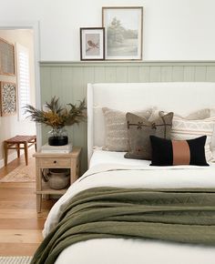 a white bed topped with lots of pillows next to a wooden table and chair in a bedroom