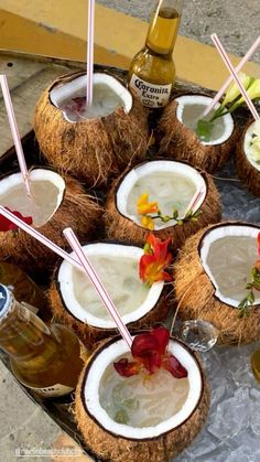 there are many drinks in coconuts on the tray with straws and flowers next to them