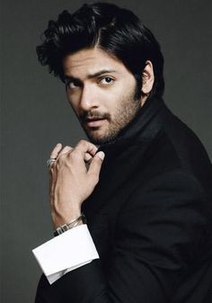 a man in a black suit and tie posing with his hand on his lapel